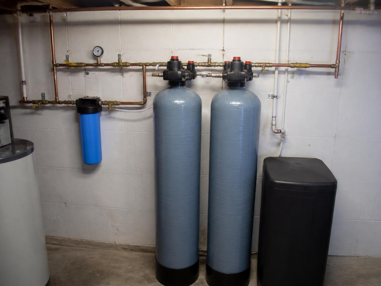 Whole-home water filtration and softener tanks plumbed along a basement wall
